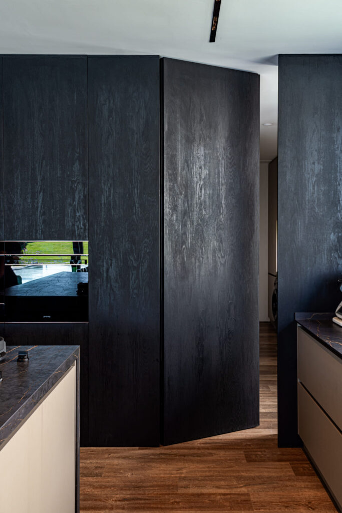 Puerta filo muro integrada en revestimiento de madera oscura.
