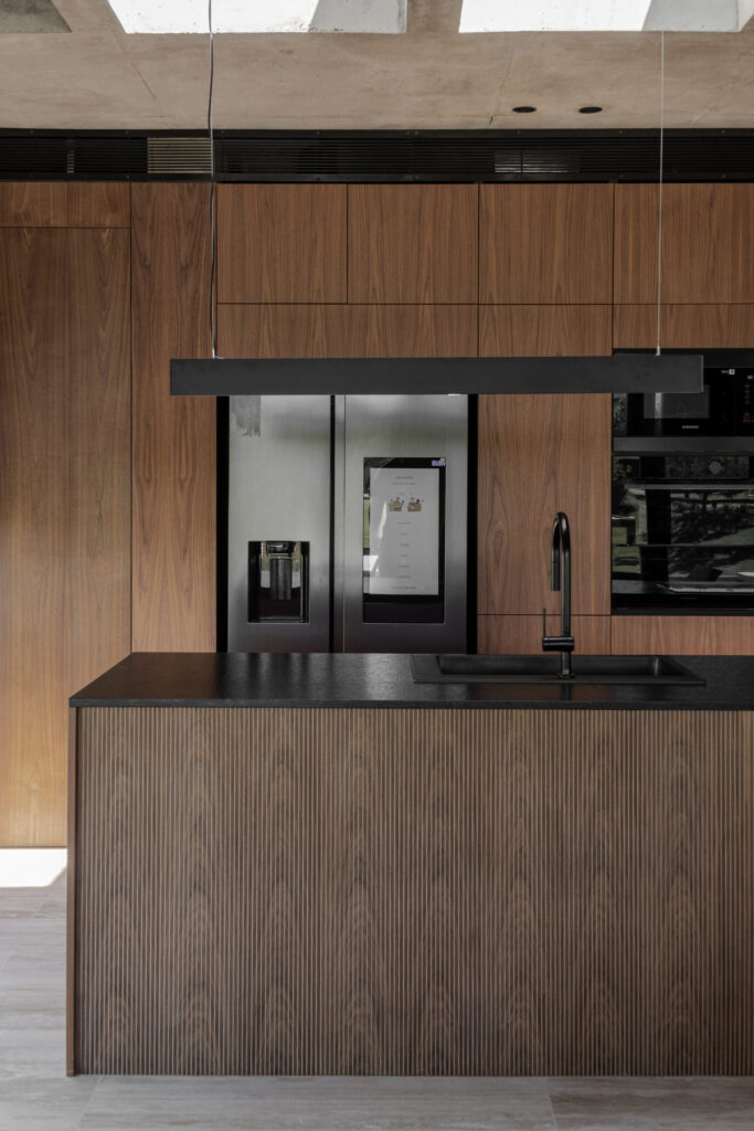 Casa Virazón II Cocina con isla central, mesada negra y revestimientos en nogal.