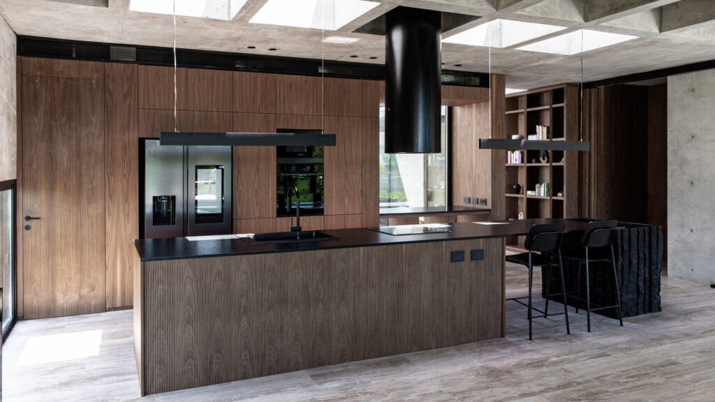 Casa Virazón II Cocina con isla central, mesada negra y revestimientos en nogal.